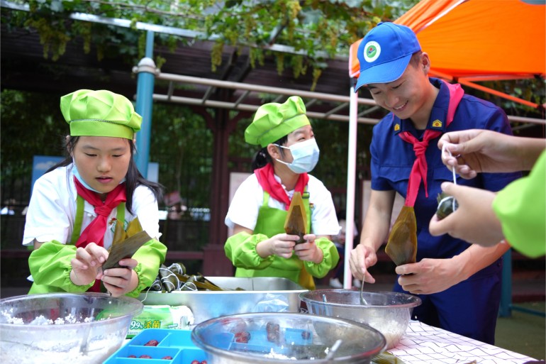 6月21日，濟(jì)南館驛街小學(xué)舉辦“皂莢樹(shù)下話端午”公益愛(ài)心主題活動(dòng)。校內(nèi)幾棵皂莢樹(shù)下，市中消防大隊(duì)的“藍(lán)朋友”們和少先隊(duì)員們一起體驗(yàn)著包粽子的時(shí)光。張?jiān)丛?陳志偉攝
