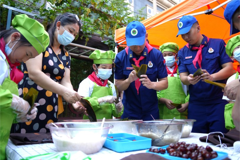 6月21日，濟南館驛街小學舉辦“皂莢樹下話端午”公益愛心主題活動。校內幾棵皂莢樹下，市中消防大隊的“藍朋友”們和少先隊員們一起體驗著包粽子的時光。張源源 陳志偉攝