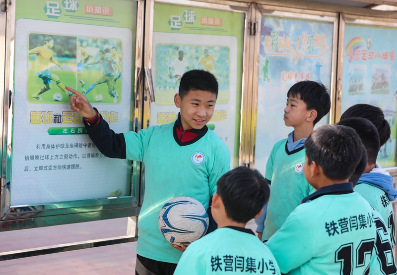 12月6日，學(xué)生們在鐵營鎮(zhèn)閆集小學(xué)足球場文化欄前分享足球知識(shí)。