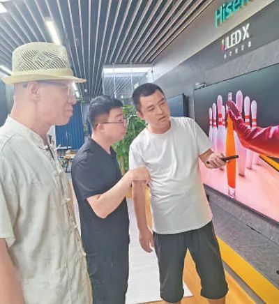 導(dǎo)購員（中）在為老王父子介紹一款智能電視。本報記者 李 蕊攝