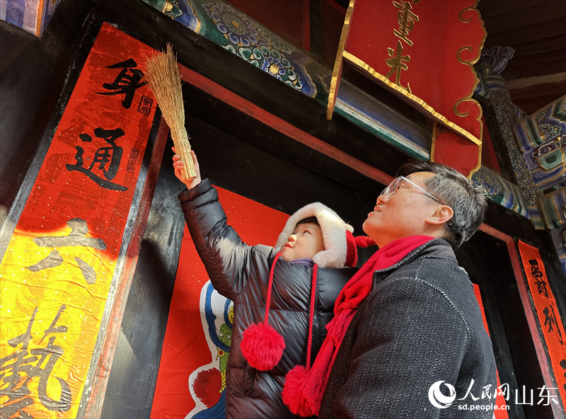 孔府重光門，孔子第77代孫孔穎（右）和孩子一起貼對(duì)聯(lián)。人民網(wǎng) 喬姝攝