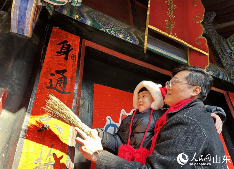 春節(jié)前，孔子后裔在孔府重光門前貼春聯(lián)。 人民網(wǎng) 喬姝攝