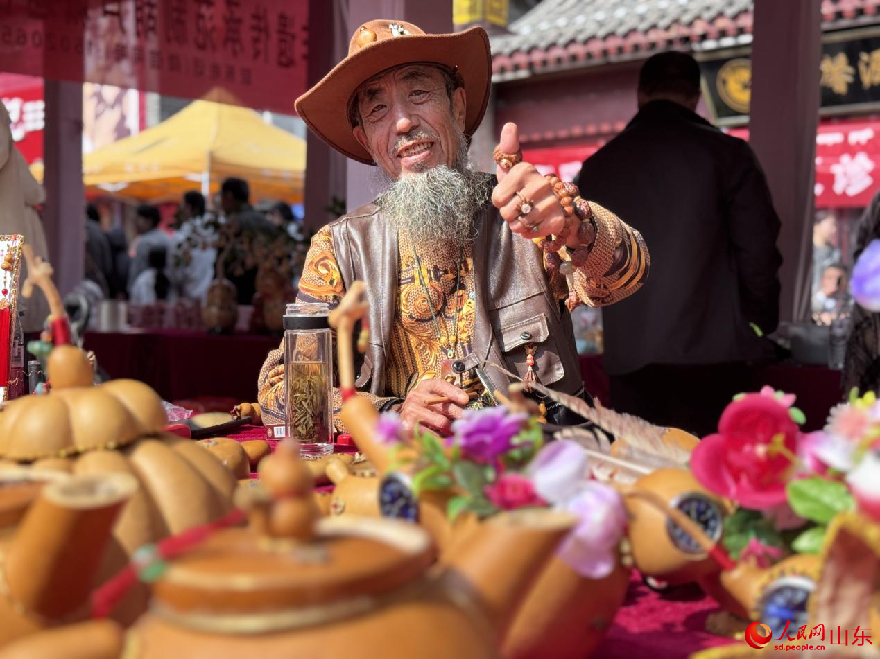 攤主大爺對自家的葫蘆工藝品十分滿意，正對著鏡頭點(diǎn)贊。人民網(wǎng) 鄭昕橋攝