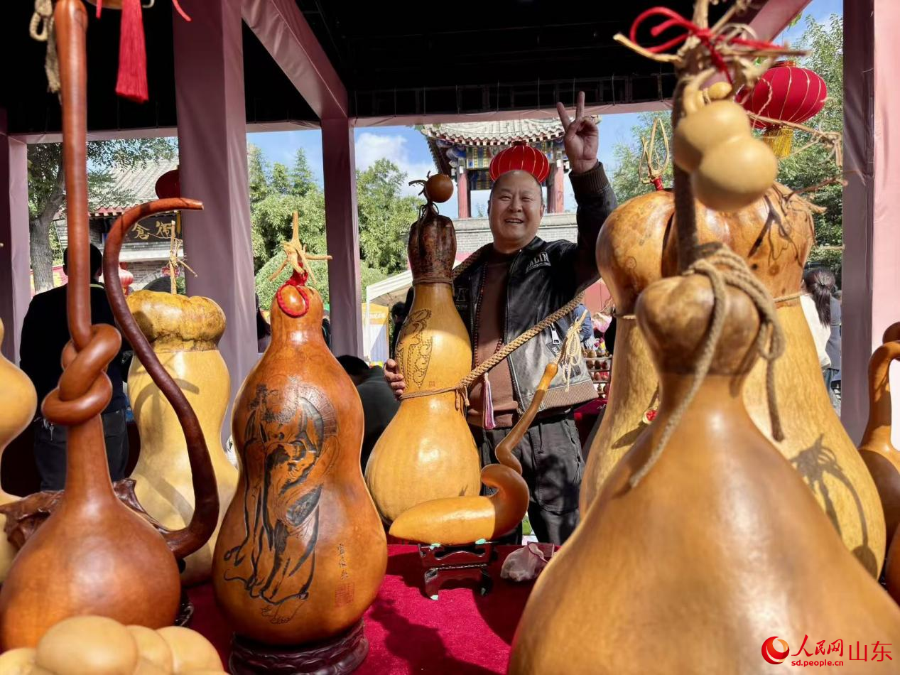 身掛大葫蘆工藝品的攤主正向游客展示自己心愛的寶貝。人民網(wǎng) 鄭昕橋攝